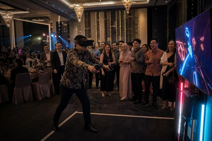 Guests at a hotel ballroom dinner and dance watch a colleague play at a VR game booth