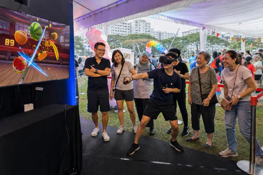A family watches a teenager play VR under a carnival tent at a company family day in Singapore