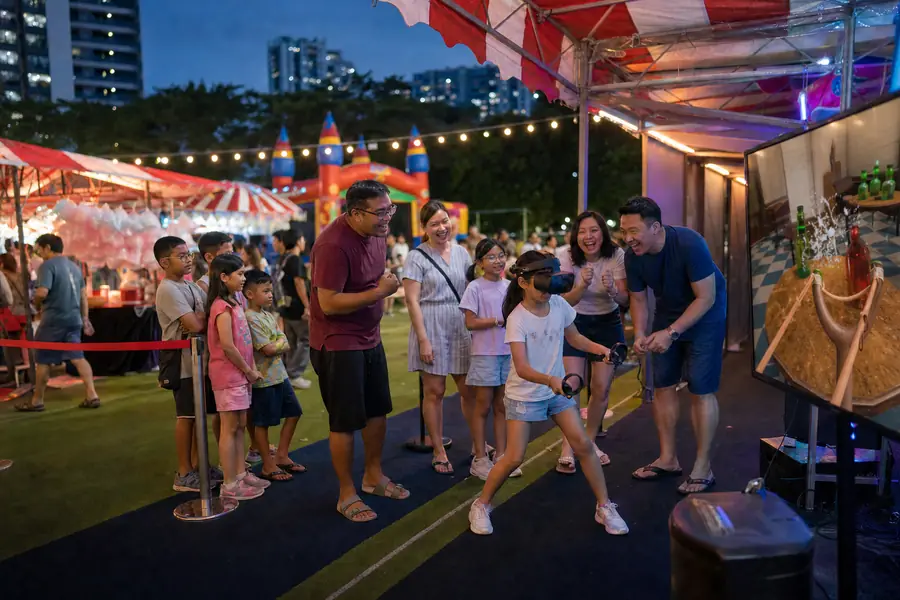 Children and parents cheer a girl playing VR at an evening carnival booth on a Singapore school field